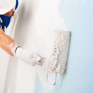 side view of  painter in white dungarees, helmet and gloves painting a wall with paint roller,  with copy space, selective focus on paint roller